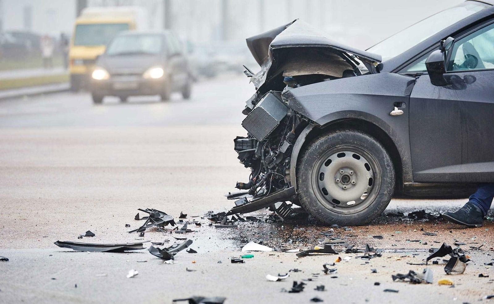 A car with severe front-end damage after a collision on a foggy road.