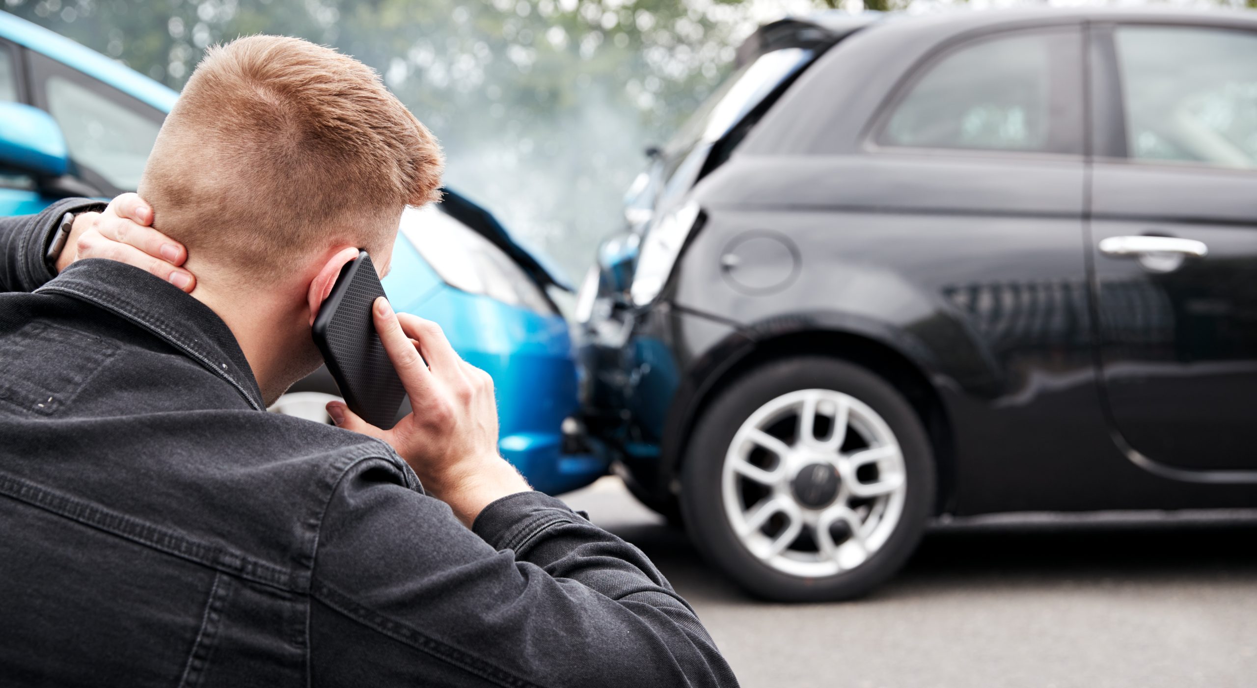 Man holding his neck and speaking on the phone after a rear-end car accident involving 2 vehicles with visible front and rear-end damage.