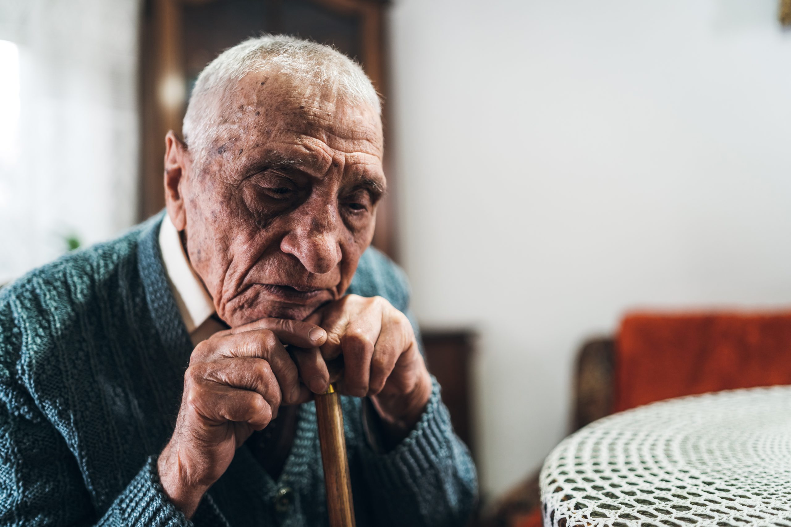Elderly man with a solemn expression resting his head on a cane.