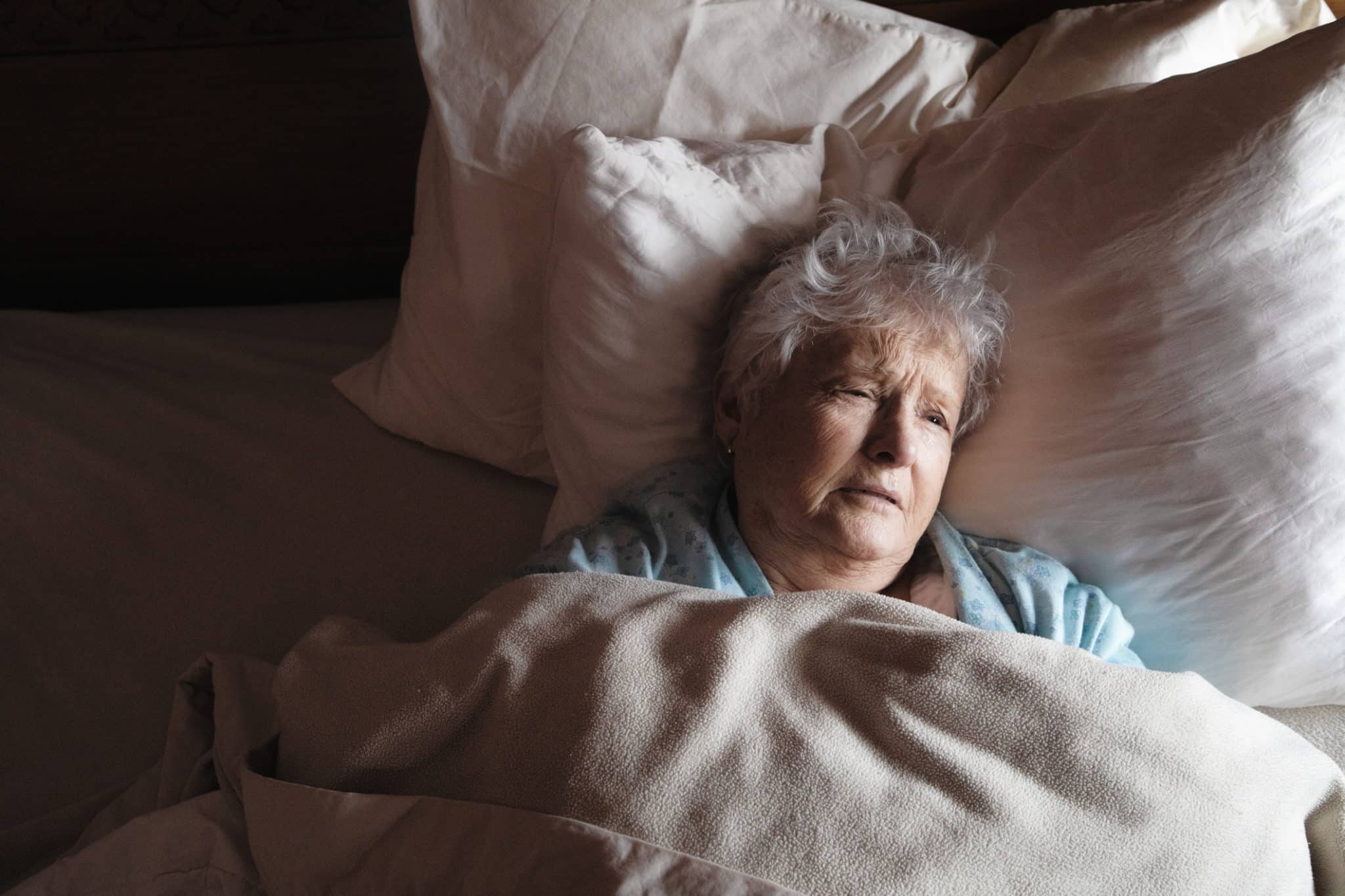 Elderly woman lying in bed with a pained expression on her face.
